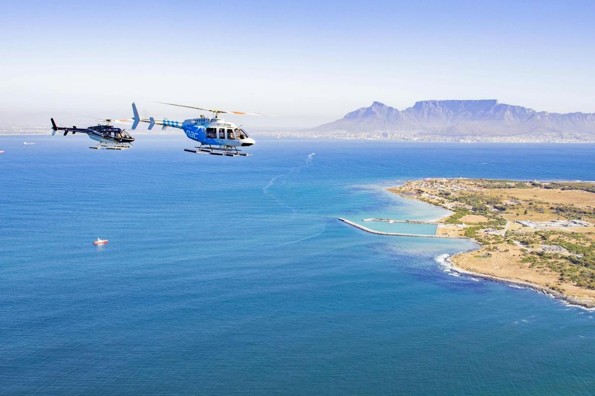 dva helikopterja letita nad vodo blizu plaže