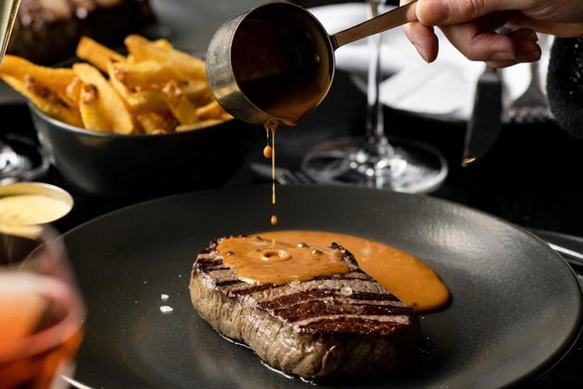 una persona che versa la salsa su una bistecca con patatine fritte