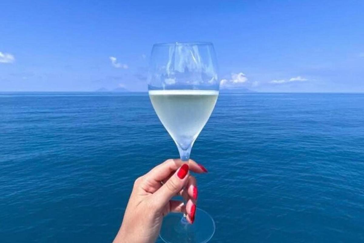 una mano che tiene un bicchiere di vino bianco sopra l'oceano