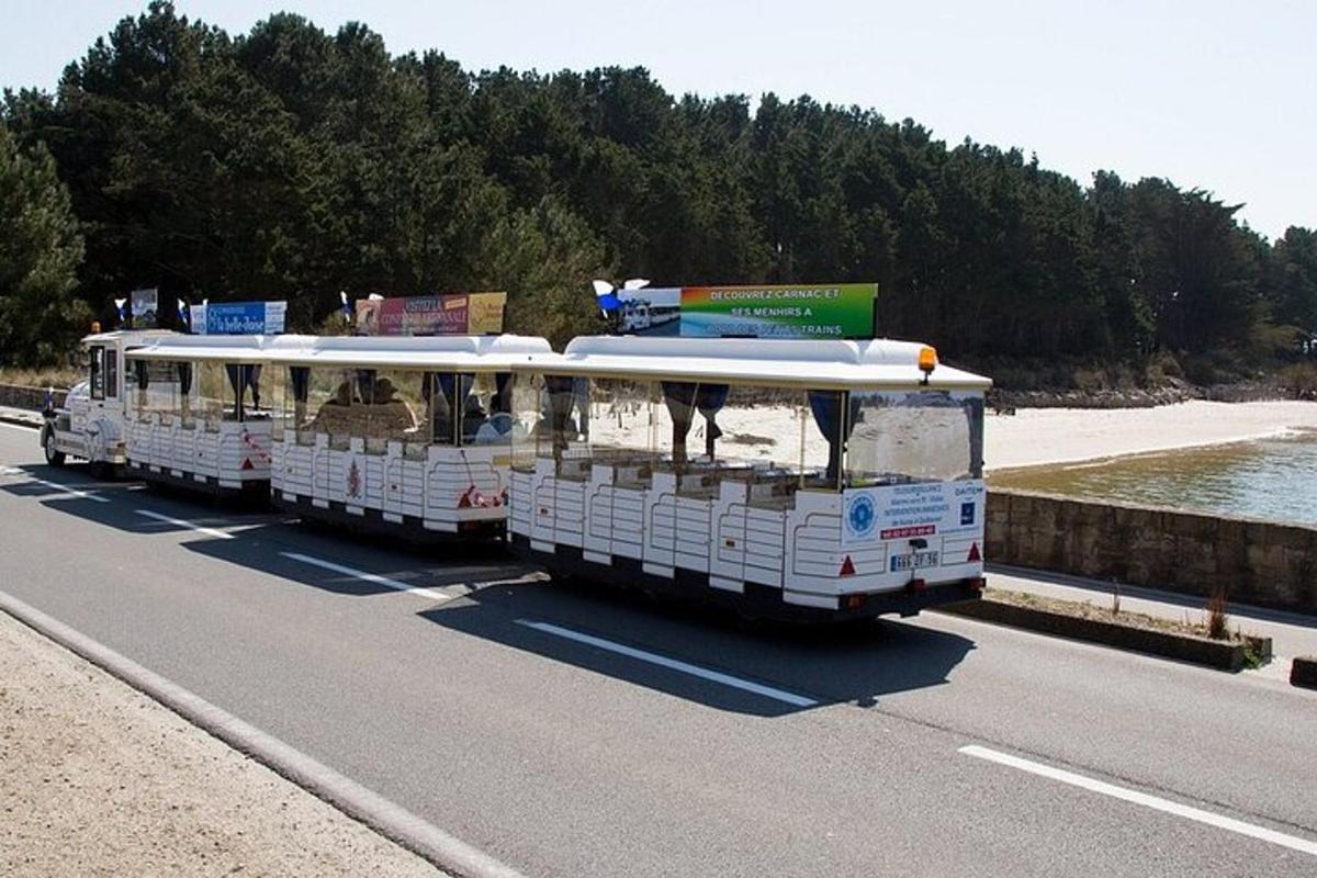 two white buses driving down a road next to a beach