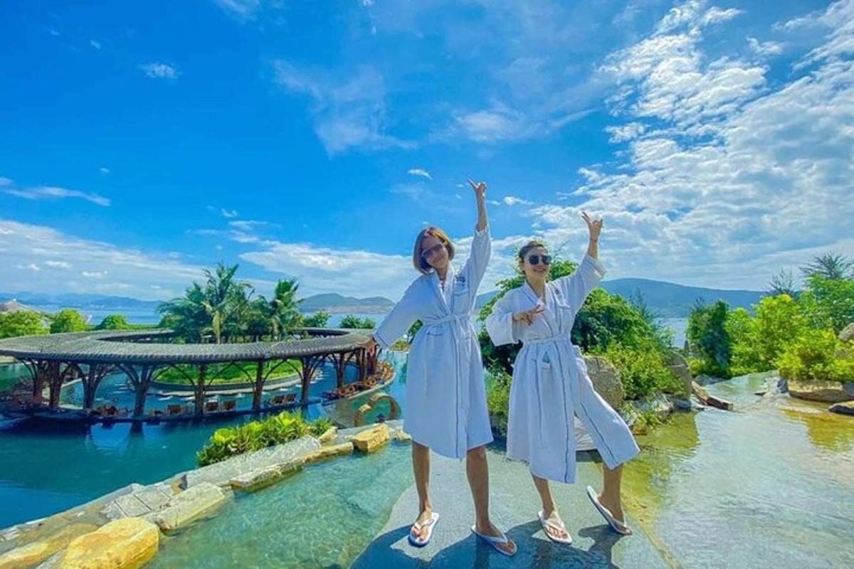 hai người phụ nữ mặc váy trắng đứng trên một tảng đá dưới nước