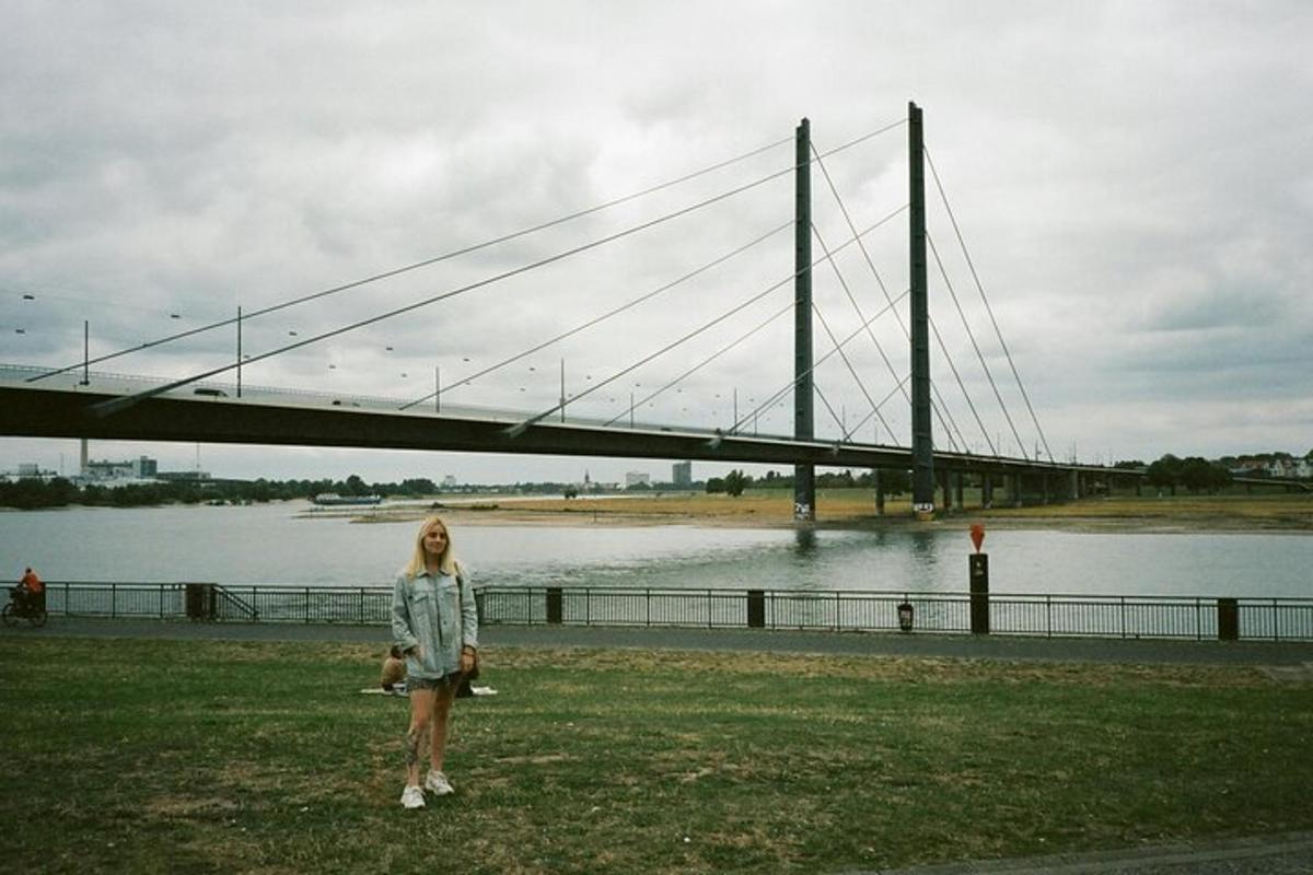 a woman standing in the grass in front of a bridge