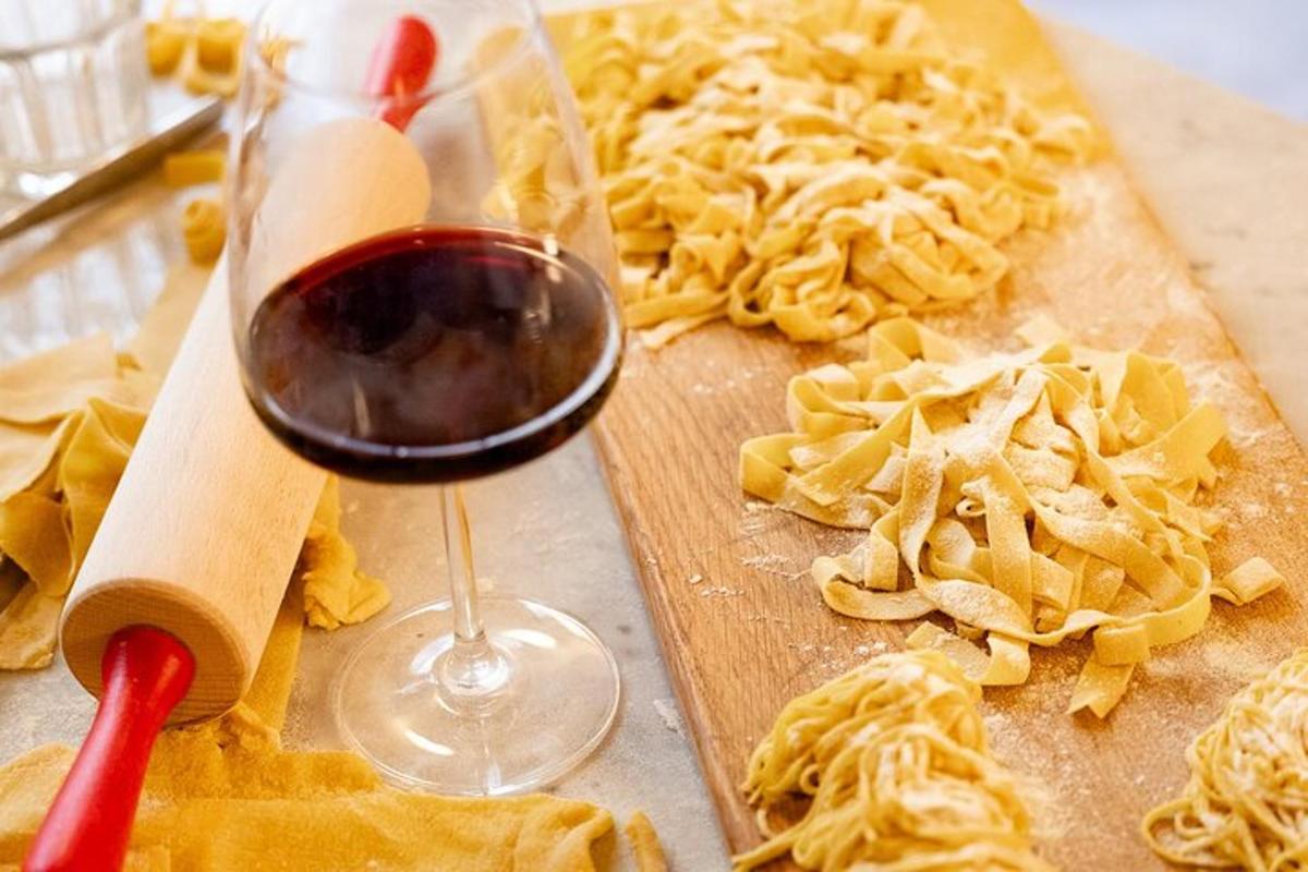 segelas wain di sebelah papan pemotong dengan pasta