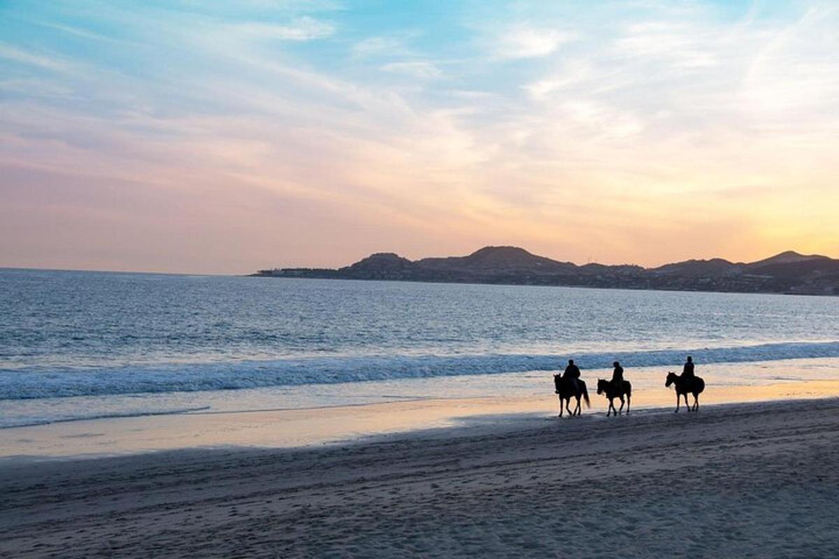 tre persone a cavallo sulla spiaggia al tramonto