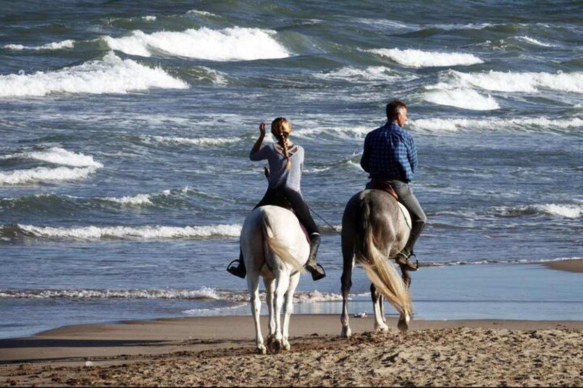 a man and woman riding horses on the beach