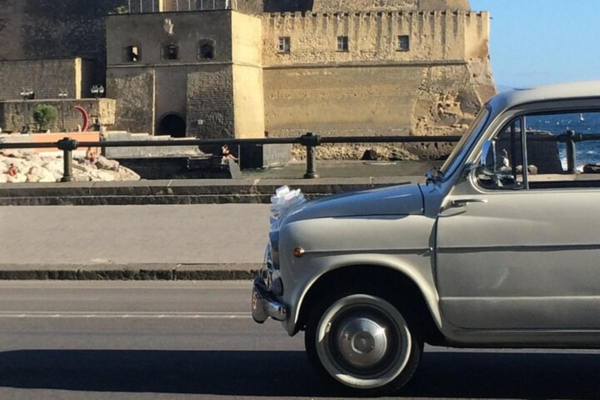 Un coche viejo circulando por una calle frente a un edificio.
