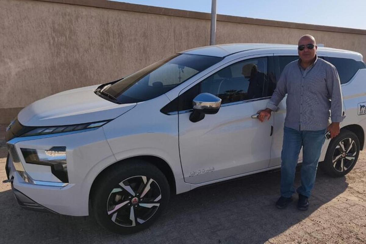 Un hombre está parado junto a un coche blanco.