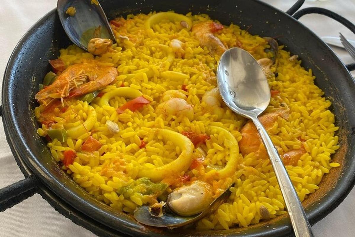 a pan filled with yellow rice with seafood and spoons