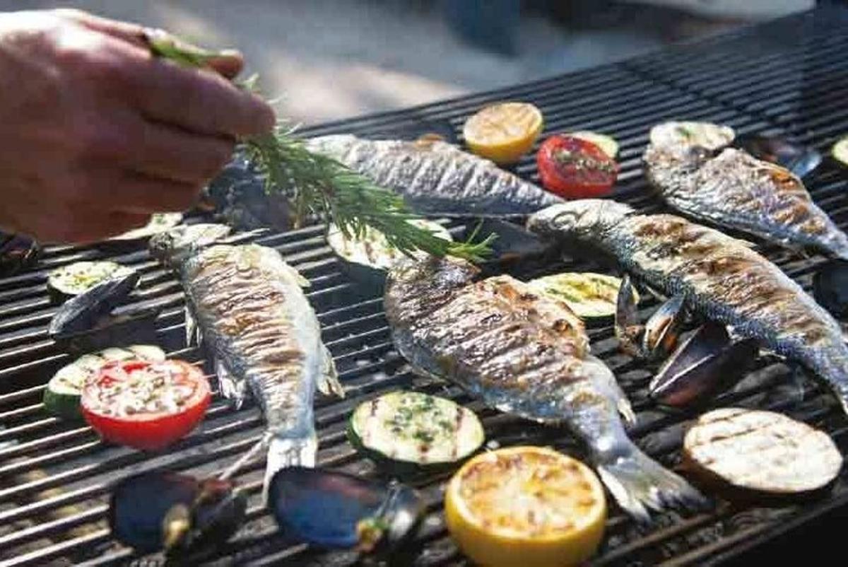 seseorang memasak ikan dan sayur-sayuran di atas panggangan