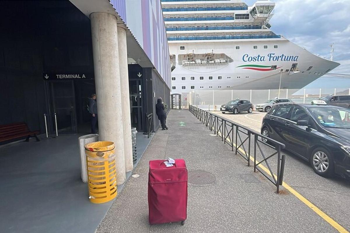a red suitcase sitting on a sidewalk next to a cruise ship