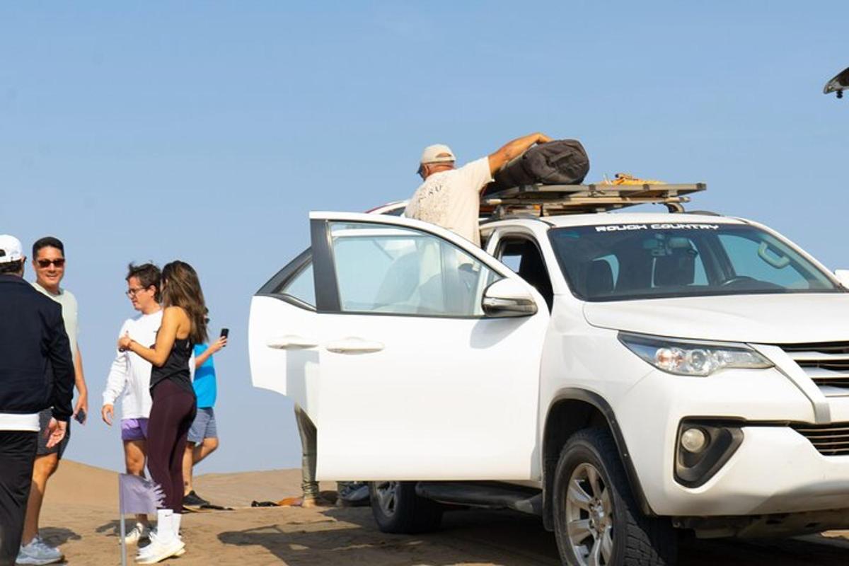 Un grupo de personas de pie alrededor de un coche blanco en la playa.