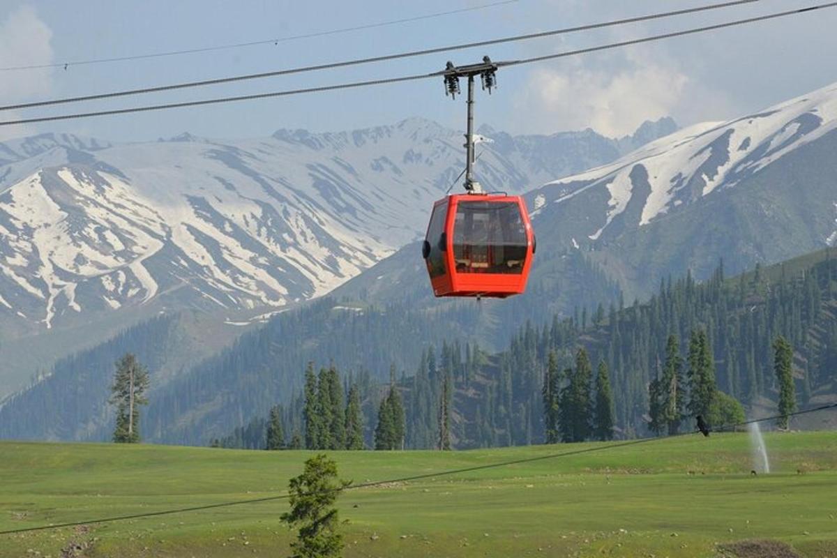 a red cable car flying over a field with snow covered mountains