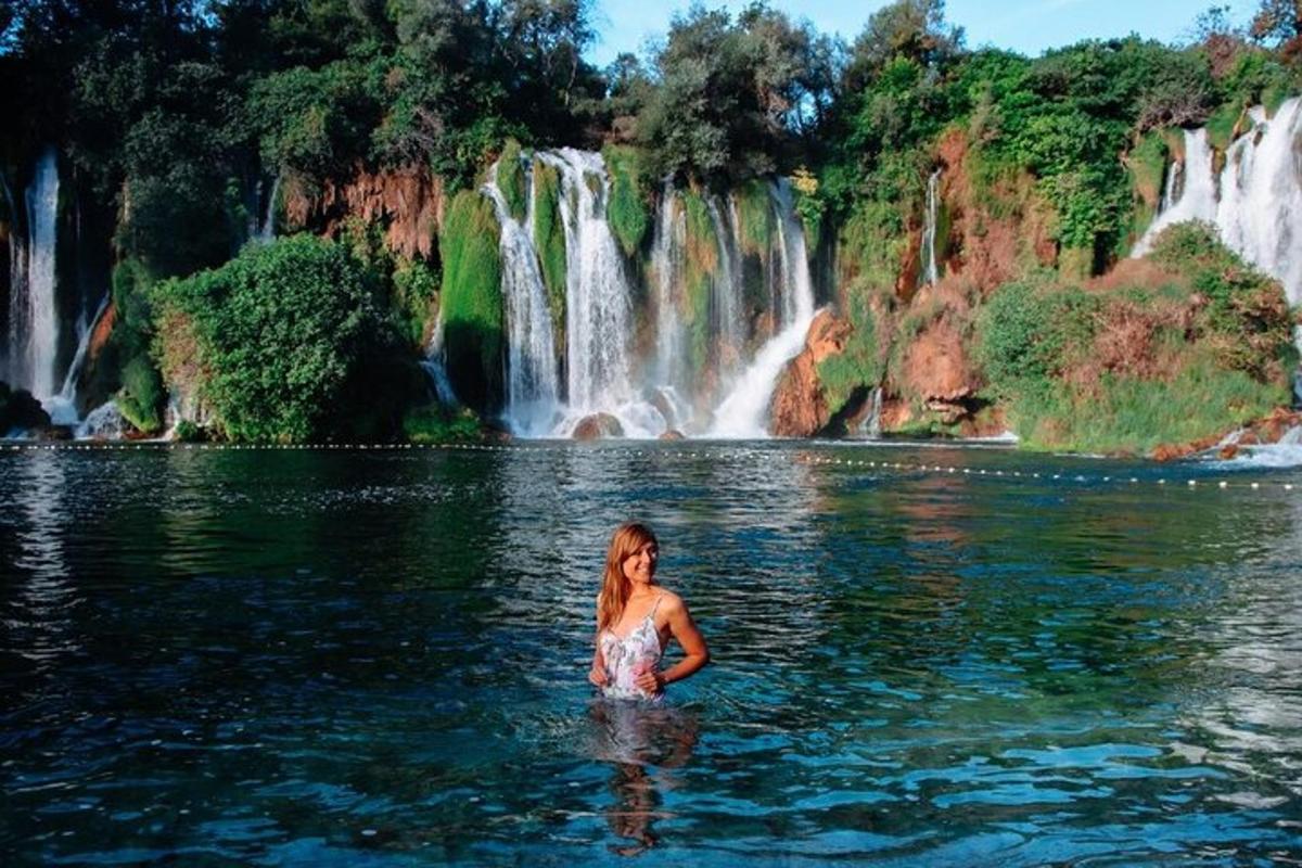 a woman standing in the water in front of a waterfall