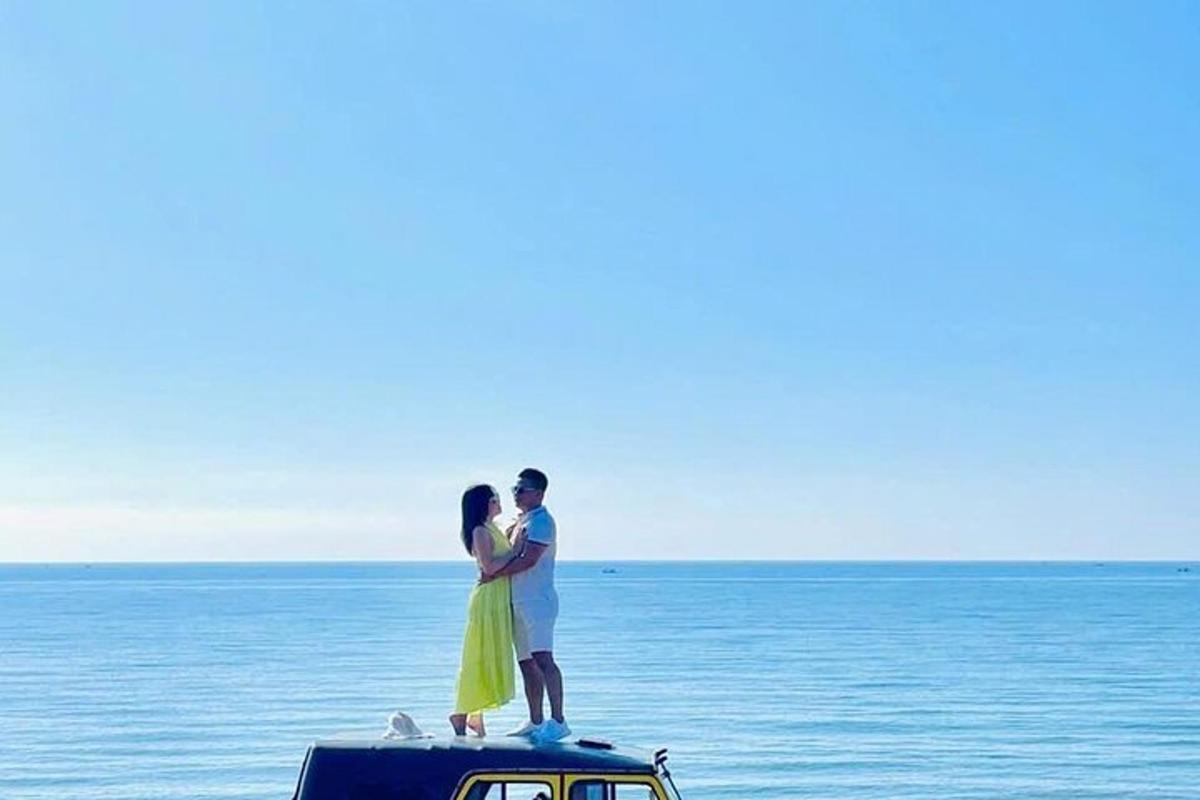 a man and a woman standing on the top of a car on the beach