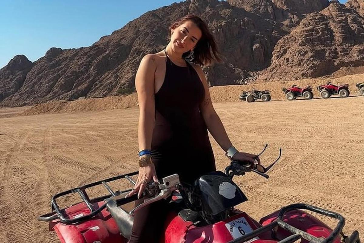 seorang wanita berdiri di sebelah motosikal di padang pasir