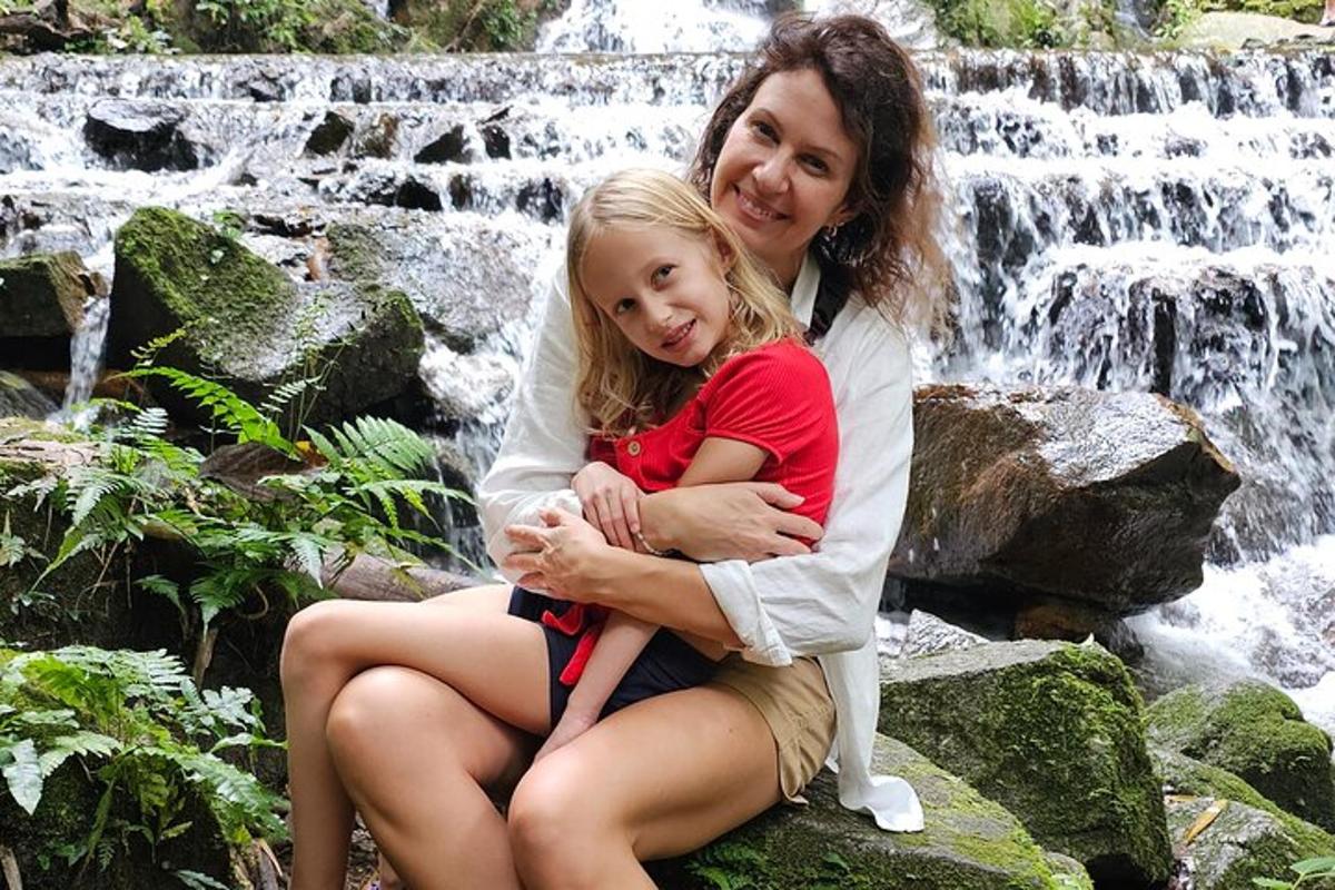 seorang wanita dan seorang gadis kecil duduk di hadapan air terjun