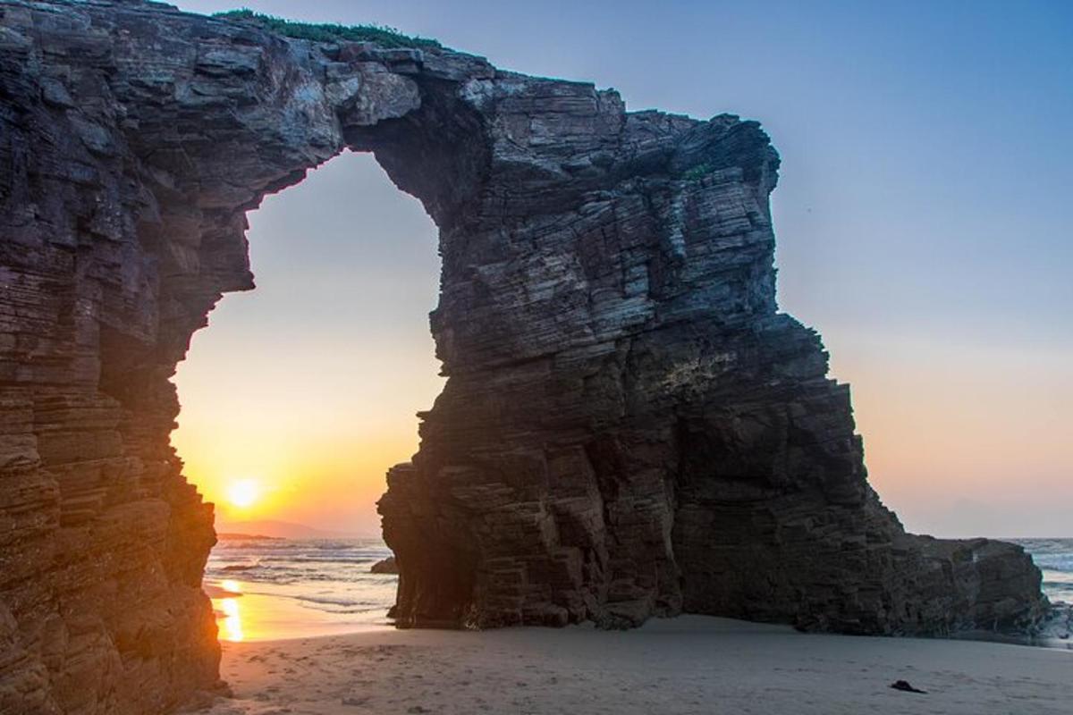 an arch in the rocks on the beach with the sunset
