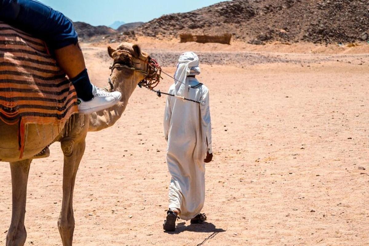 um homem caminhando com um camelo no deserto