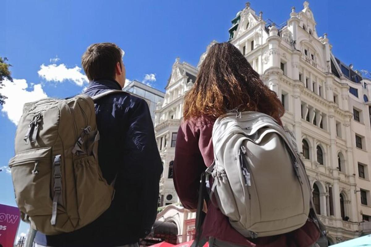 Dos personas con mochilas de pie frente a un edificio.