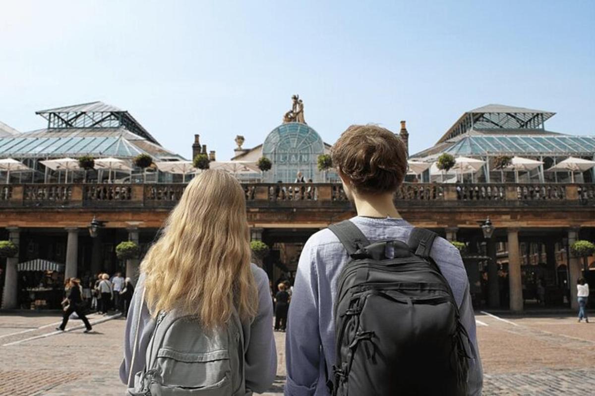 Dos personas con mochilas de pie frente a un edificio.