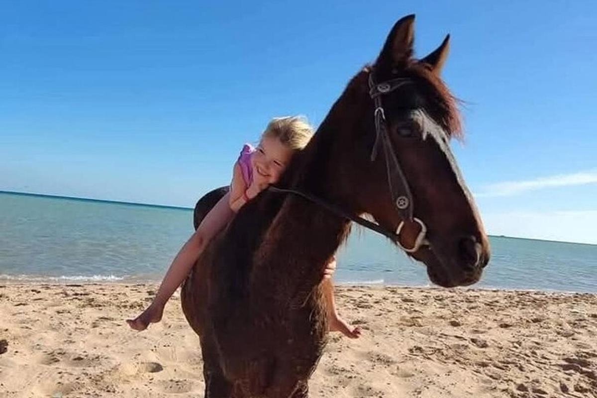 una noia jove muntant a cavall a la platja