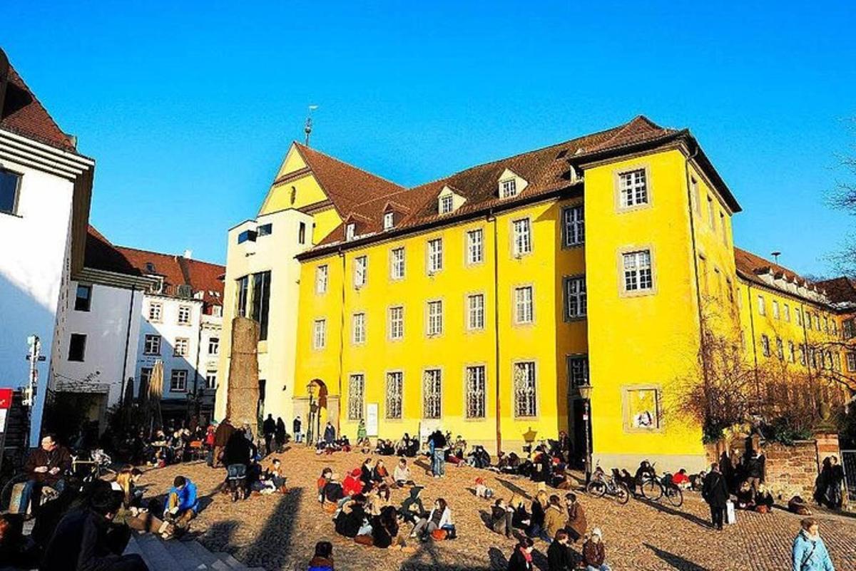 grupp inimesi istub kollase hoone ees