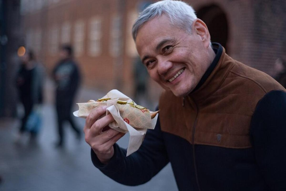 un uomo anziano che mangia un hot dog per strada