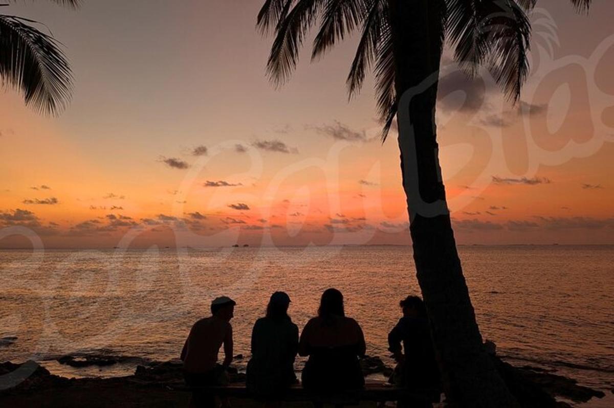 skupina ljudi, ki sedijo na plaži in opazujejo sončni zahod