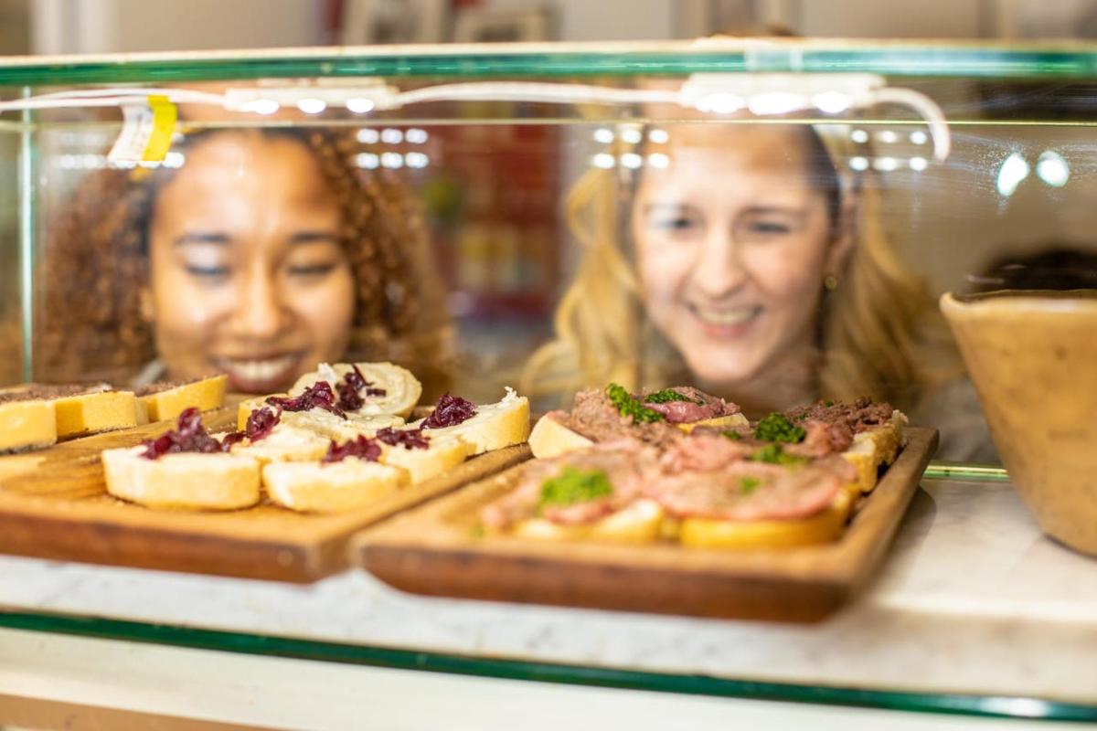 dvě ženy za skleněnou vitrínou s pizzami