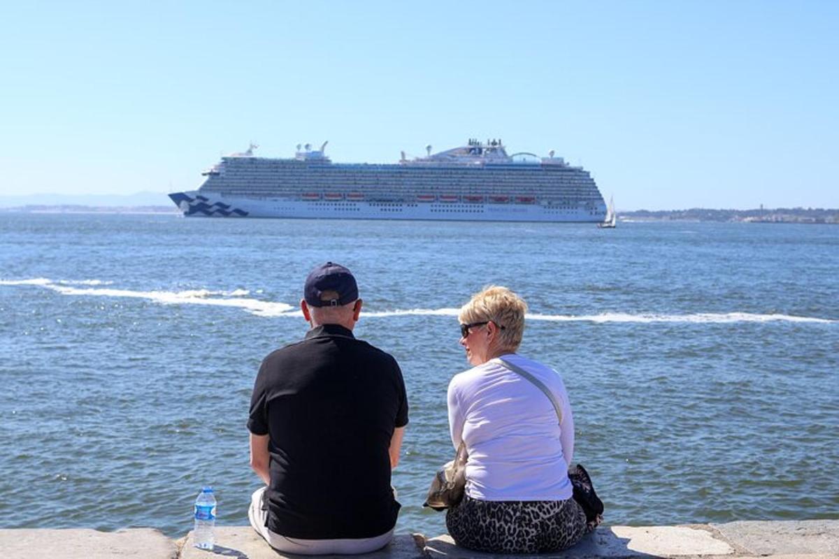 Ein Mann und eine Frau sitzen auf einem Felsvorsprung und schauen auf ein Kreuzfahrtschiff