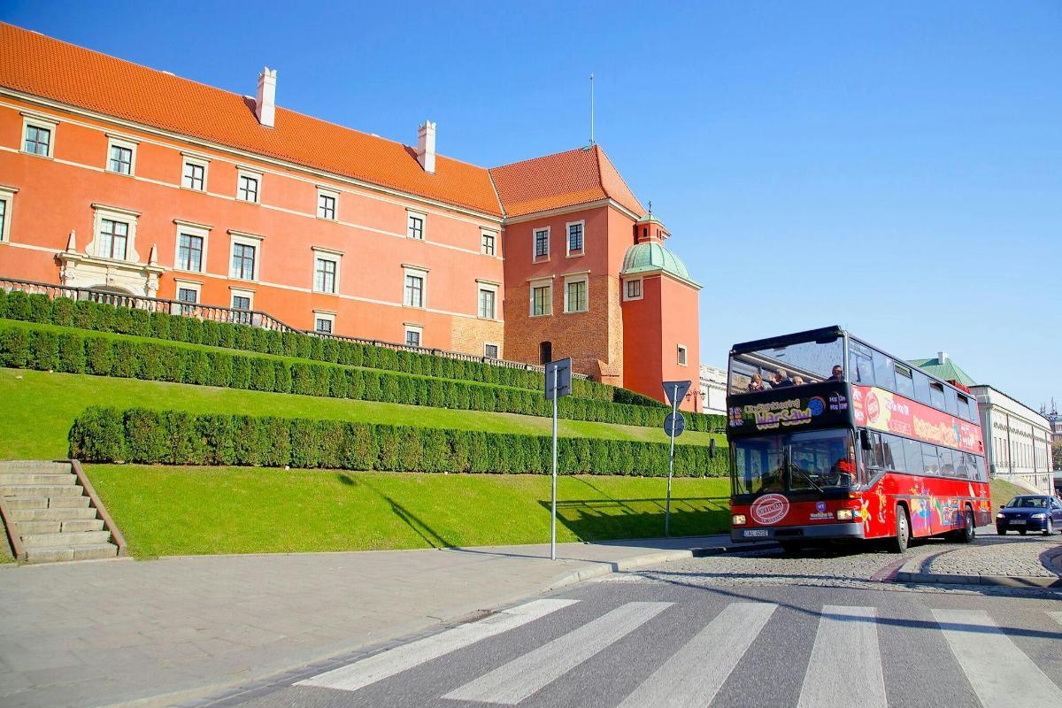 a red double decker bus driving past a building