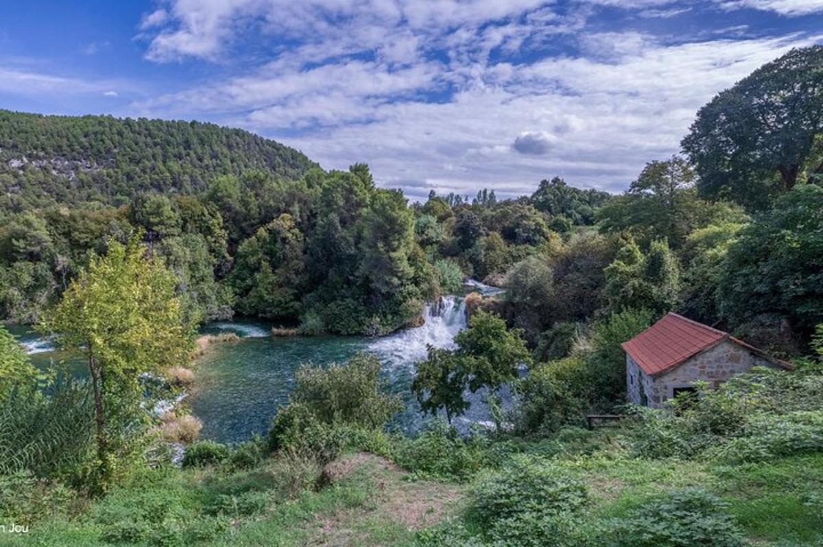 upe mežā ar māju un ūdenskritumu