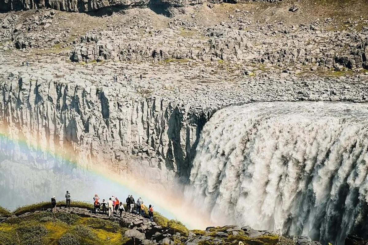 sekumpulan orang berdiri berhampiran air terjun dengan pelangi