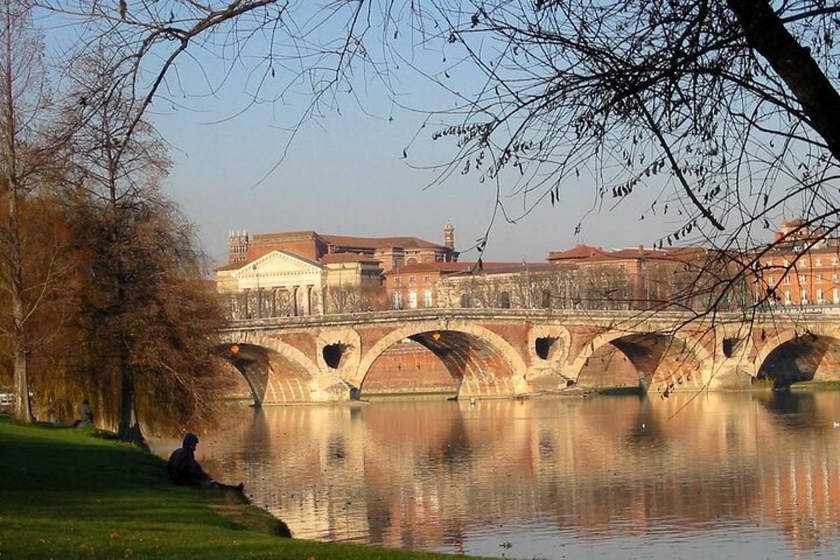 Un hombre sentado en el césped junto a un puente.