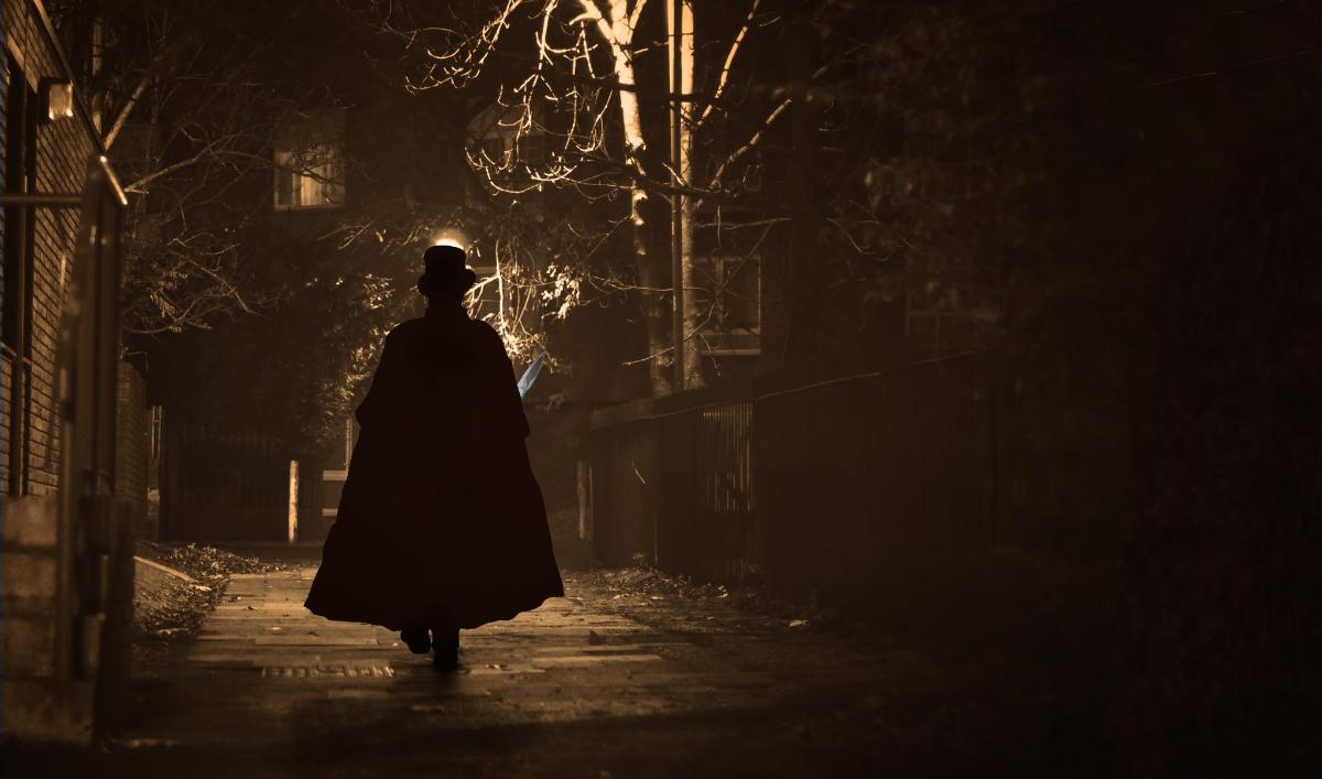 osoba w płaszczu idąca nocą ulicą