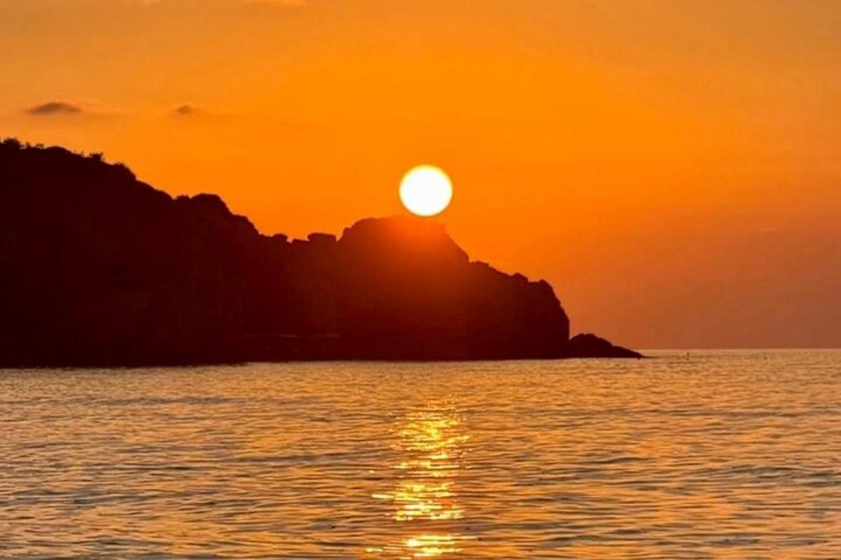 Ένα πορτοκαλί ηλιοβασίλεμα πάνω από τον ωκεανό με ένα βραχώδες νησί