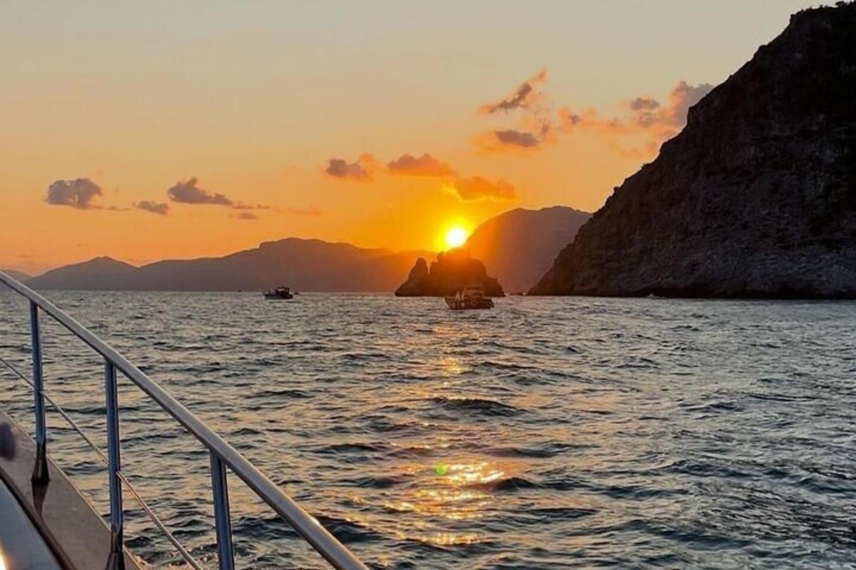 μια βάρκα στο νερό με τον ήλιο να δύει πίσω από τα βουνά
