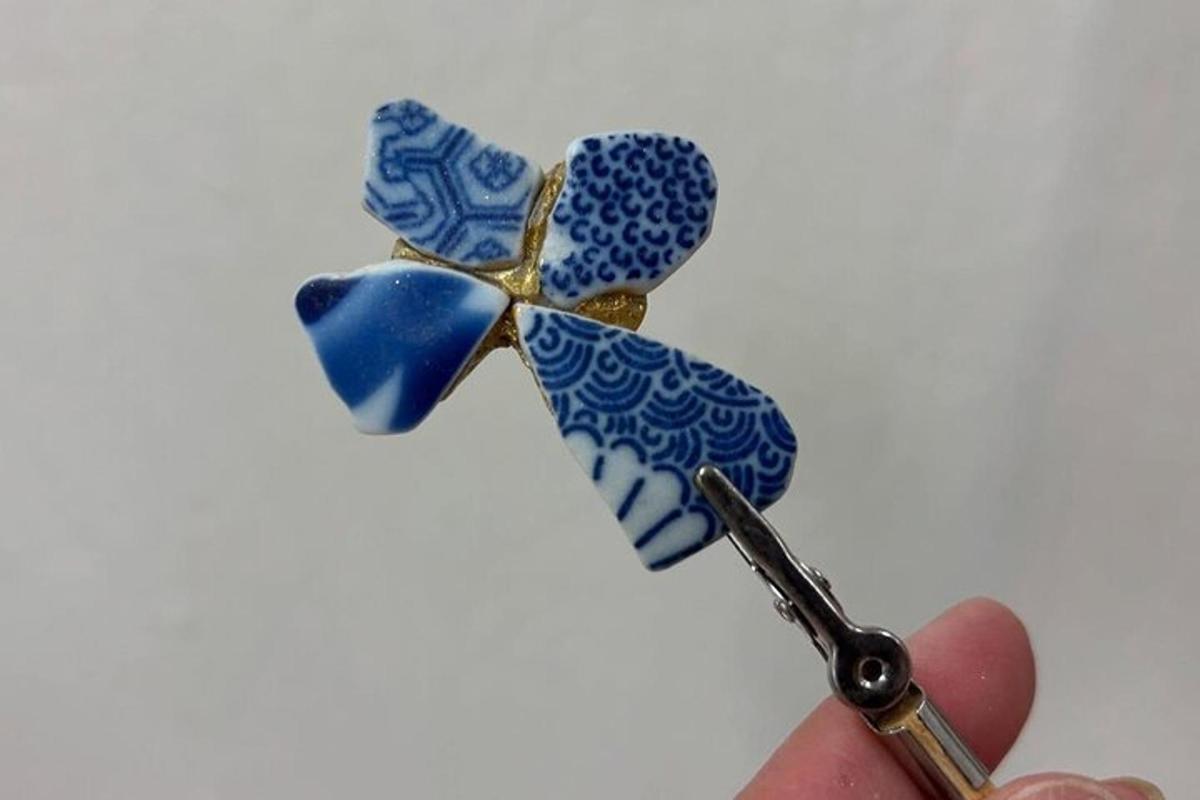 tangan memegang sepasang gunting dengan kerongsang berwarna biru