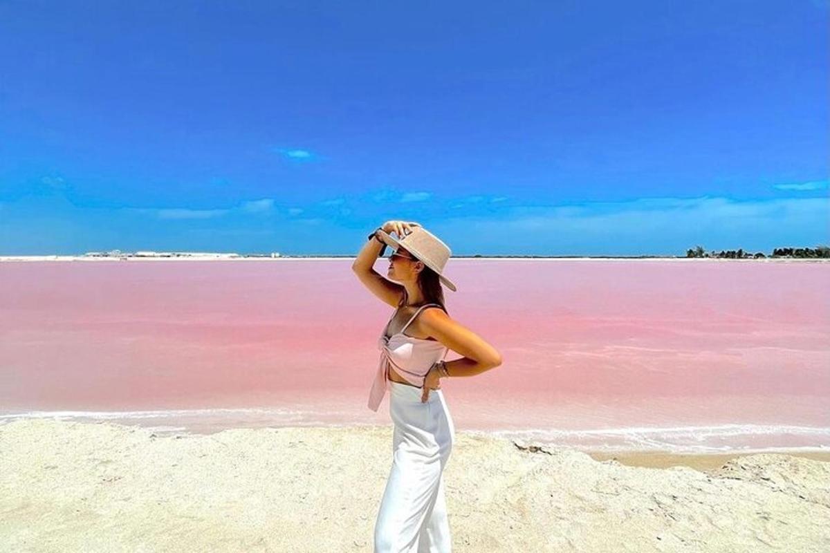 Una mujer parada en una playa con un lago rosa.