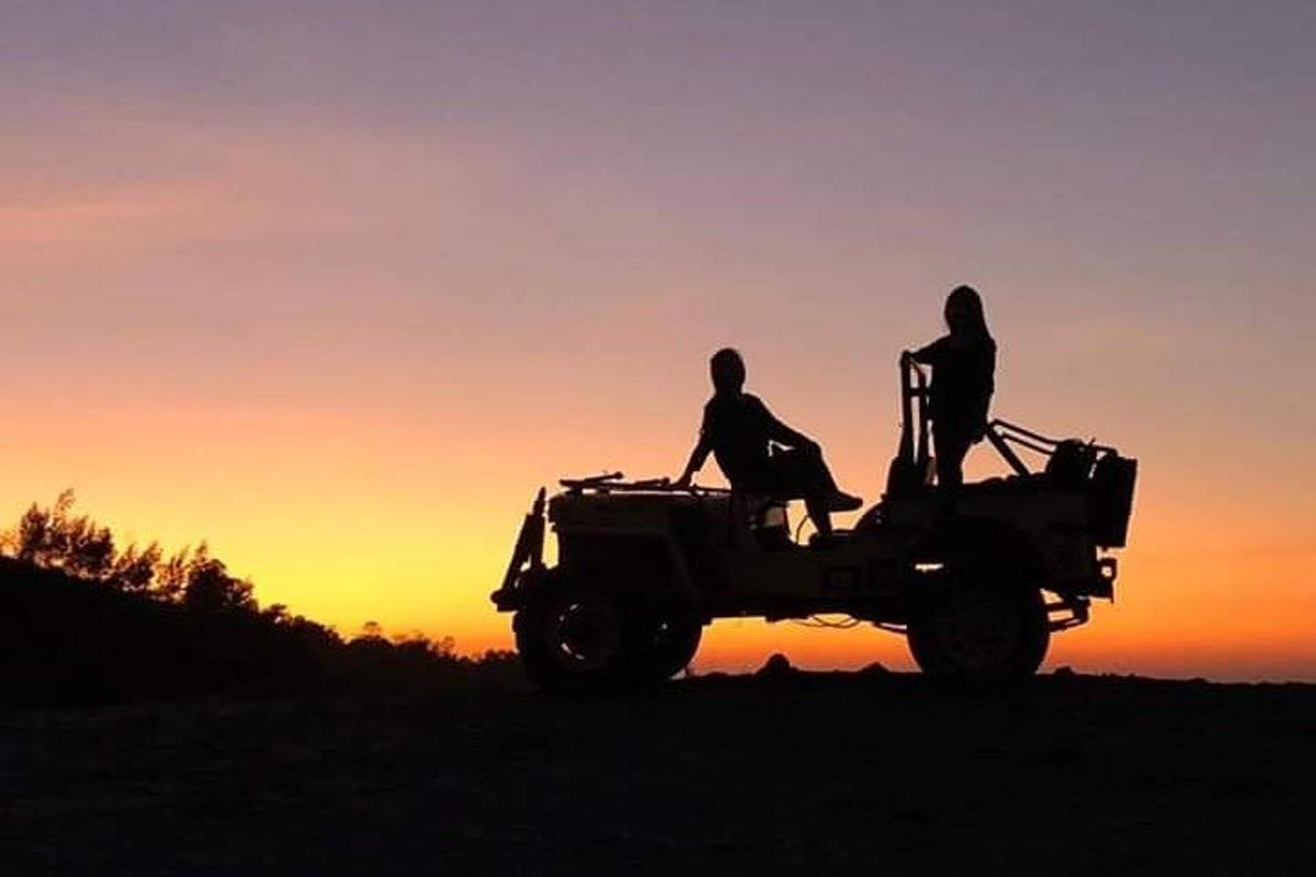 duas pessoas sentadas no topo de um jipe ao pôr do sol