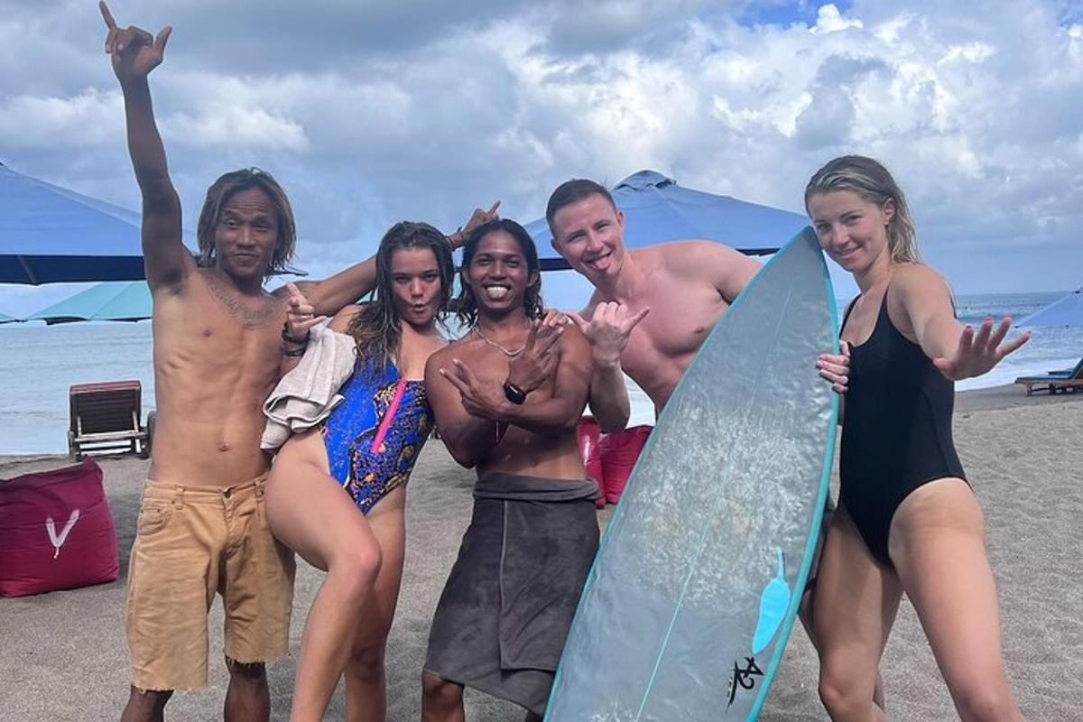 sekelompok orang berdiri di pantai dengan papan selancar
