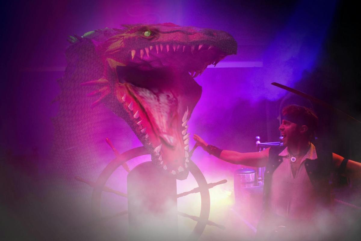 a woman standing next to a dinosaur head on a stage
