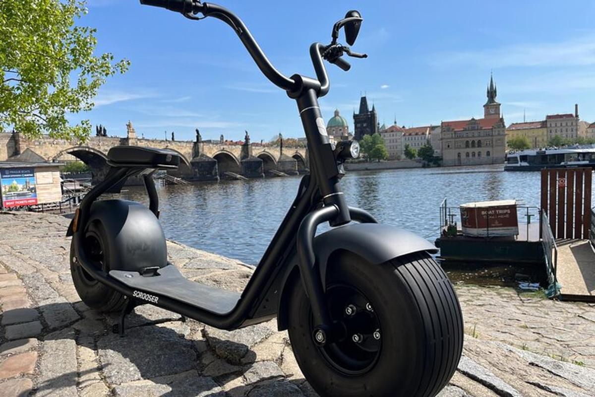 skútr zaparkovaný vedle řeky s mostem