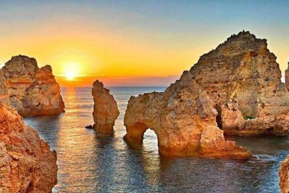 a sunset over the ocean with rocks in the water