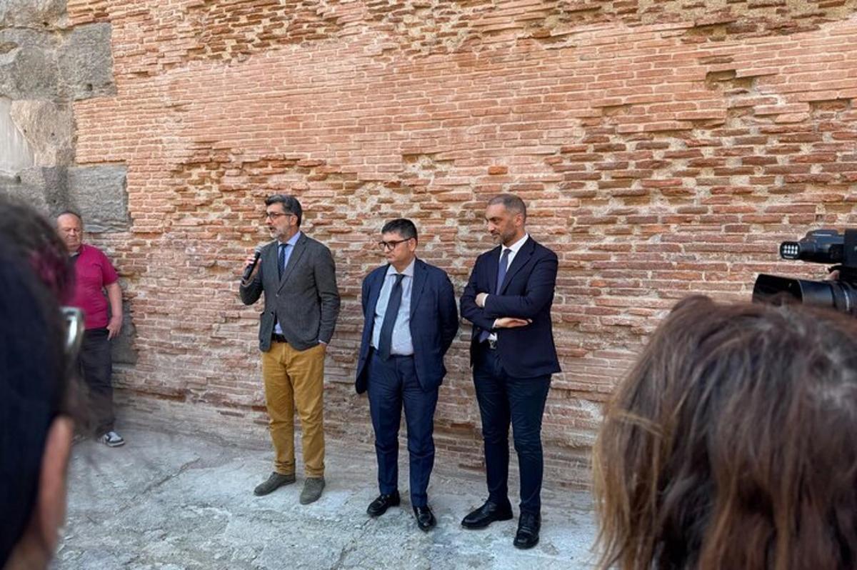 tatlong lalaking naka-suit na nakatayo sa harap ng isang brick wall