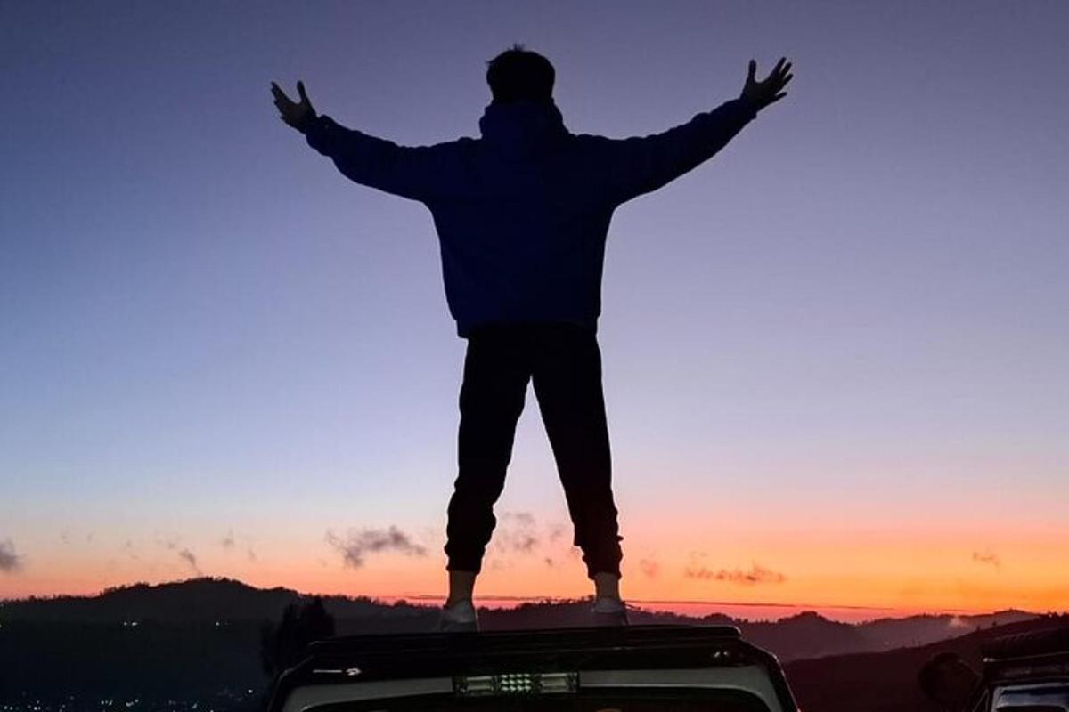 um homem em pé no topo de um veículo com os braços estendidos