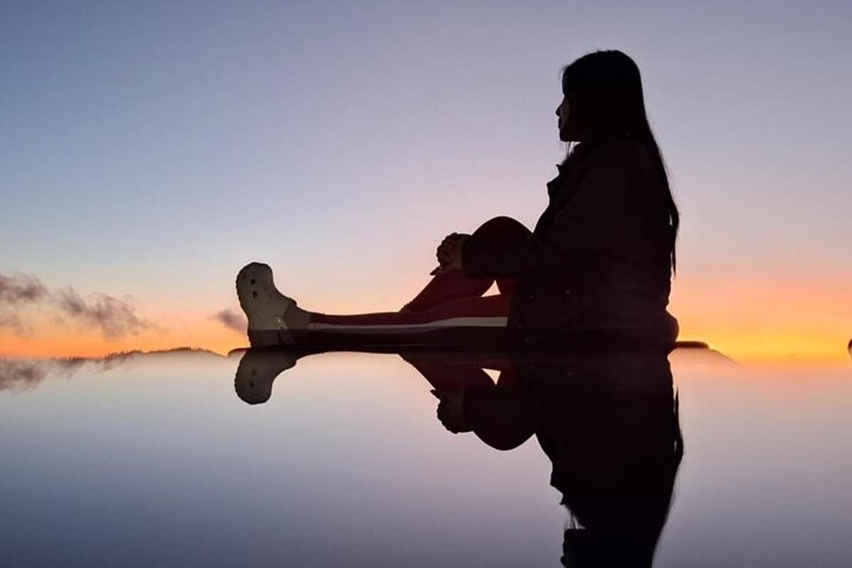 uma mulher sentada em um barco na água ao pôr do sol