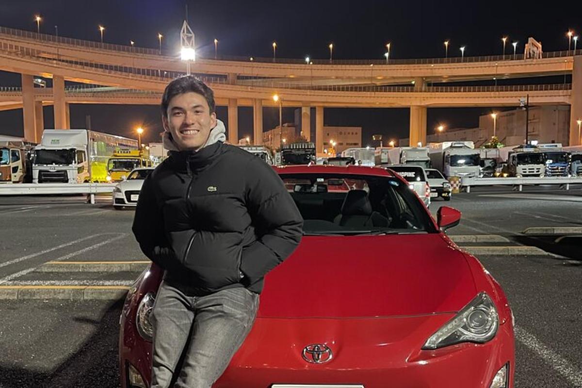 seorang lelaki berdiri di sebelah sebuah kereta berwarna merah