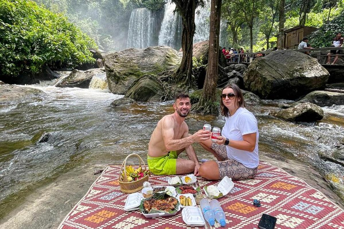 Un hombre y una mujer sentados en una manta de picnic junto a una cascada.