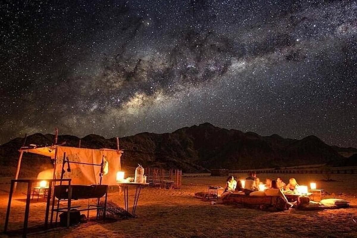 Un grupo de personas sentadas alrededor de una tienda de campaña bajo un cielo estrellado.
